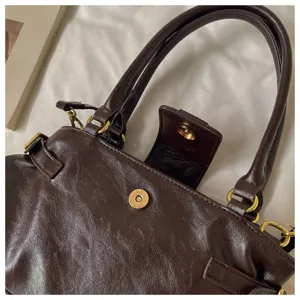 Primer plano del bolso de cuero marrón oscuro con botón a presión metálico y detalles.