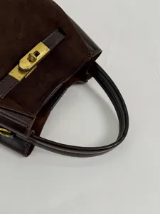 Detailopname van donkerbruine suède en lederen handtas met klassiek goudkleurig metalen slot.