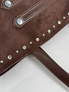 Close-up detail of brown suede handbag with metallic silver rivets and leather strap.