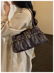 Detalle de bolso de hombro estilo moto vintage, cuero PU marrón oscuro con hebillas y tachas.
