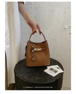 Detailopname van een retro bruine suèdé emmertas met gouden draaisluiting en kraalhangers.