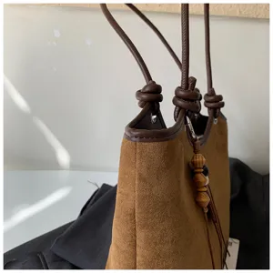 Brown suede bucket bag detail shot, featuring knotted leather handles and wooden bead pendant.