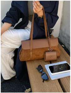 Brown leather suede shoulder bag detail view with hanging pouch, lifestyle scene on wooden bench.