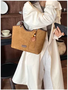 Detailed view of vintage brown suede tote bag with leather badge and chic wooden charm decor.