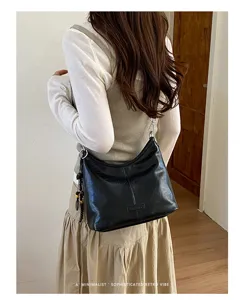 Minimalist black leather hobo shoulder bag detail, stylish dumpling bag for women, chic retro vibe.