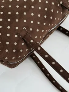 Gros-plan du sac à main marron à pois blancs, affichant une texture douce et une fermeture éclair chic.