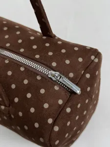 Gros plan sur les détails d'un sac Boston à pois bruns montrant sa fermeture éclair douce.