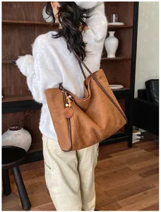Close-up of a brown suede shoulder tote bag with cute charm, worn by model indoors.