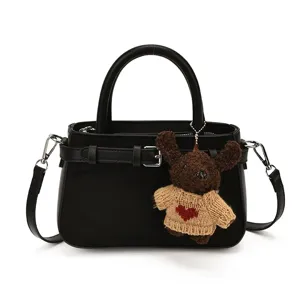 Stylish black leather shoulder handbag with cute knit bear pendant for daily wear.