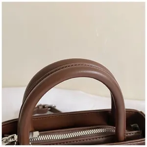 Detailed view of brown leather handbag handle and silver zipper, sleek commuting bag close up