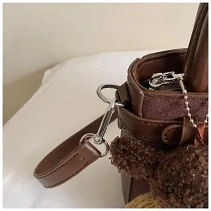 Close-up detail of brown leather shoulder bag hardware and cute plush bear pendant ornament.