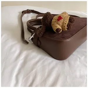 Detailed shot of trendy brown suede women handbag with cute bear charm, chic daily commuter crossbody.