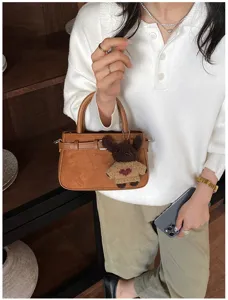 Close-up detail of stylish brown suede handbag with cute knitted bear pendant for daily wear.