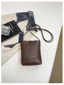 Detail shot of dark brown minimalist leather bucket bag with slim strap and stylish design.