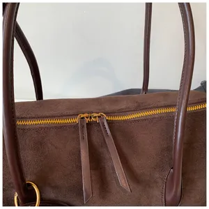 Primer plano detallado del bolso de hombro de ante marrón con cremallera doble.