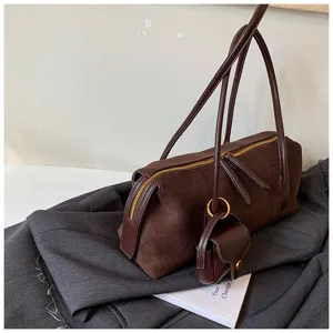 Bolso de hombro de ante marrón bajo el brazo con monedero colgante y cremallera dorada.