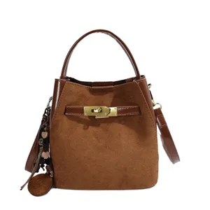 Brown suede bucket bag for women stylish crossbody handbag with metal lock and chic charm pendant.