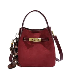 Burgundy suede bucket bag with leather trim, metal lock closure and wooden bead charm.