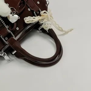 Λεπτομερής όψη σκούρας καφέ τσάντας με λουλούδια, δαντελωτό φιόγκο και κρεμαστό κόσμημα.
