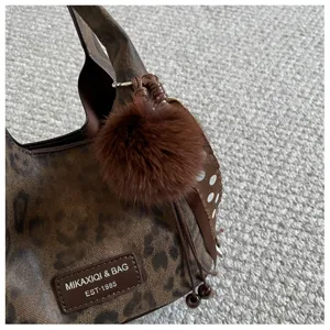 Exquisite Detailansicht der braunen Handtasche mit Leopardenmuster und flauschigem Plüsch-Anhänger.