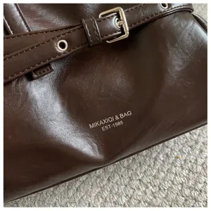 Dark brown PU leather shoulder bag detail shot featuring metal buckle and brand logo print.