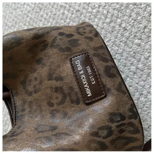 Detailansicht des braunen Leopardenmuster Damen Handtasche Stoffes und Markenetikett.