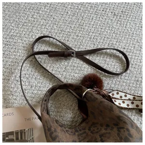 Detailaufnahme der trendigen braunen Umhängetasche mit Monogramm-Textur und Pelzanhänger.