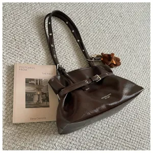 Brown leather shoulder bag detail, stylish buckle design with cute bear pendant charm accessory.
