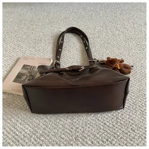 Detailed view of dark brown leather tote bag with shoulder strap and cute bear keychain.