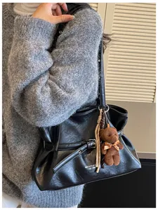 Close-up detail of black leather tote shoulder bag with stylish belt and cute teddy bear.