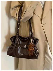 Dark brown leather shoulder bag detail with buckle strap, grommet accents and cute bear pendant.