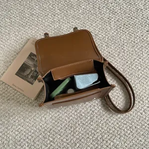 Gedetailleerd overzicht van bruine retro PU lederen schoudertas open op tapijt met boek