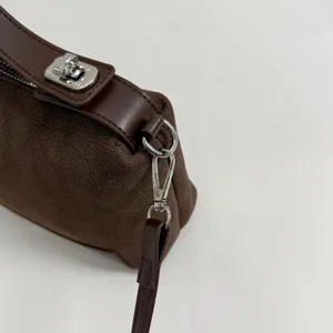 Close-up detail of brown suede handbag featuring silver metal hardware and clasp, stylish.