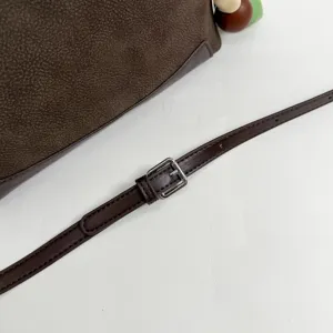 Close-up detail of brown leather shoulder bag strap with silver buckle and cute beads.