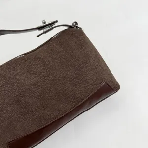 Close-up detail of brown textured shoulder bag showing smooth leather trim and metal clasp hardware.