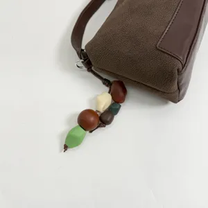 Brown suede leather shoulder bag detail showing geometric paneling and colorful bead charm.