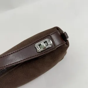 Close-up detail of a dark brown suede handbag with silver metal turn-lock and leather strap.