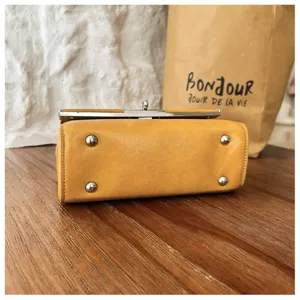 Detailed view of yellow leather handbag bottom with metal feet and neat stitching.