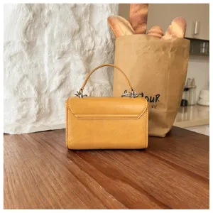 Detailed shot of yellow textured top handle handbag on wooden table with bread bag prop.