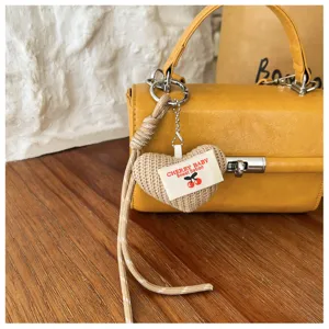 Detailed view of fashionable yellow women handbag with woven heart charm and metallic lock accent.