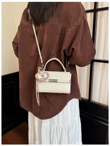 Stylish women's white shoulder crossbody bag with elegant turn-lock and cute cherry pendant.