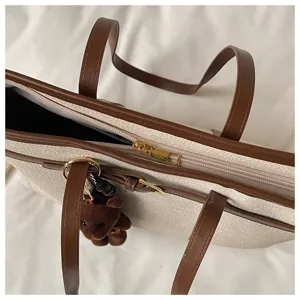 Close-up of stylish large capacity contrast tote bag with plush bear charm for daily commute.