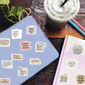Close-up flatlay of inspirational quote stickers placed on a laptop and notebook.