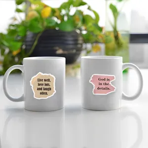 White ceramic coffee mugs set with inspirational quote stickers, minimalist desk decor detail view.