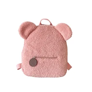 Primer plano de la mochila rosa de felpa con orejas de oso, textura de forro polar suave.