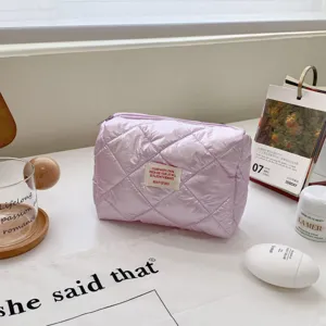 Quilted cosmetic bag detail, light purple shiny fabric with small patch, soft lifestyle aesthetic.