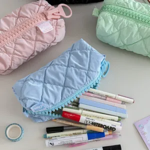 Detail shot of quilted cosmetic travel pouch with oversized zipper and colorful pens inside.