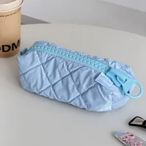 Light blue quilted cosmetic bag with oversized zipper, stylish travel makeup storage pouch.