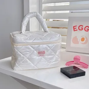 Close-up detail of white quilted puff cosmetic bag with shiny finish, stylish hand luggage design.