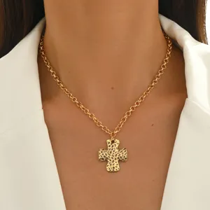 Detailed shot of gold hammered cross necklace pendant worn with white blazer, elegant style.